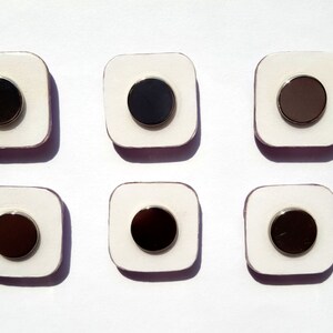 May include: Six white square tiles with a black circle in the center of each tile. The circles have a silver rim.