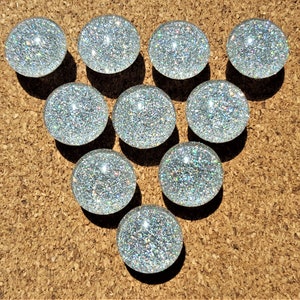 May include: Nine silver glitter push pins arranged in a triangle shape on a corkboard.