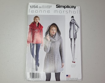Può includere: Cartamodello Simplicity 1254 di Leanne Marshall per le taglie 4, 6, 8, 10, 12. La busta presenta illustrazioni di un cappotto con cappuccio e una giacca con ampio colletto, mostrando opzioni di design per capispalla in tessuto rosso e grigio.