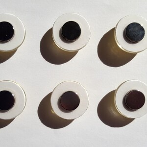 May include: Six white round magnets with black centers. The magnets are arranged in two rows of three.