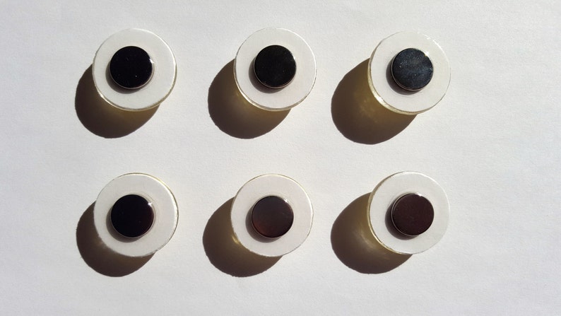 May include: Six white round magnets with black centers. The magnets are arranged in two rows of three.
