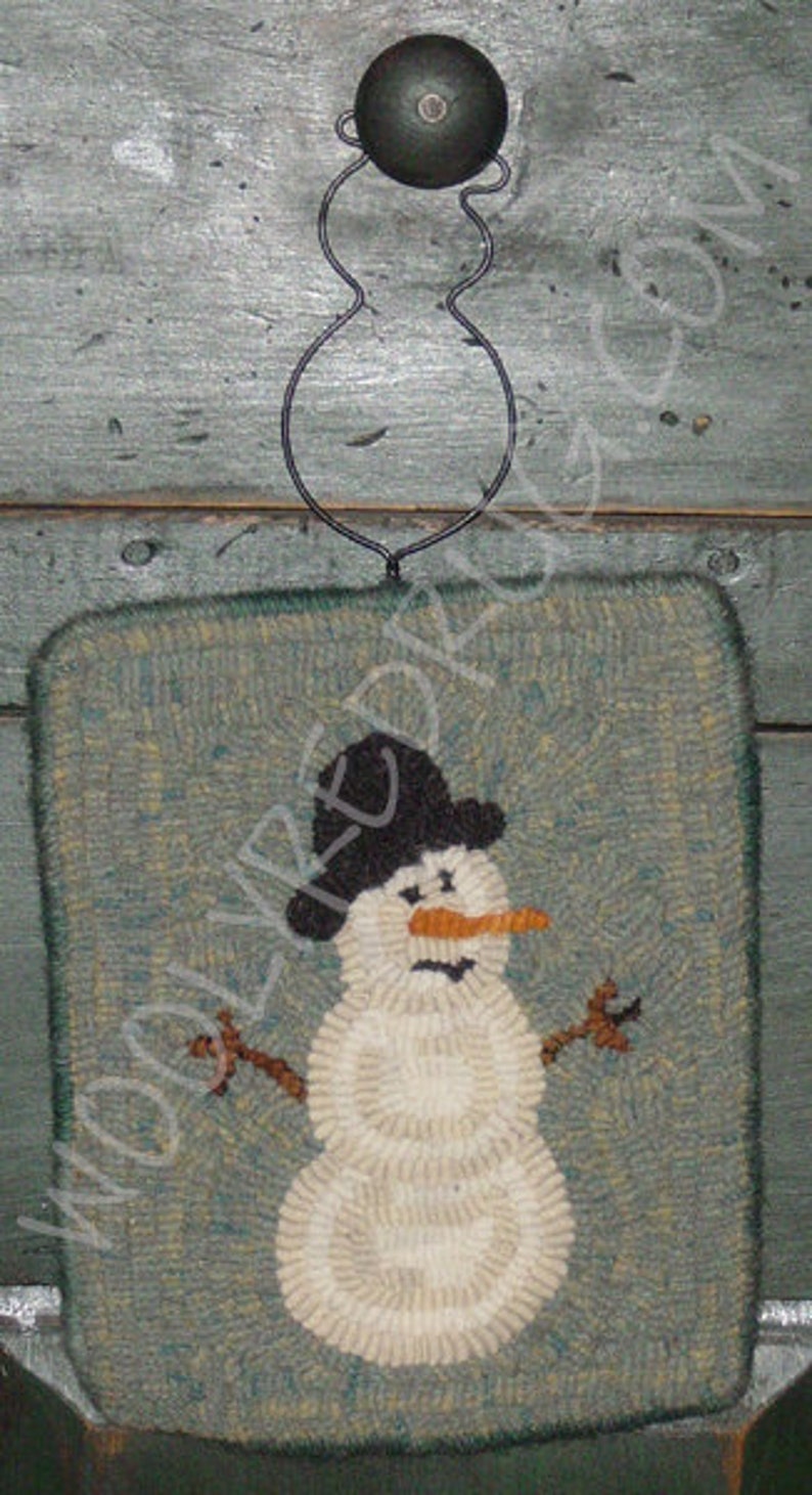 May include: A hand-hooked, square wall hanging featuring a snowman design. The snowman has a black top hat, an orange carrot nose, and twig arms. The background is a muted teal color, and the snowman is made of off-white yarn. A black metal hanger is attached.