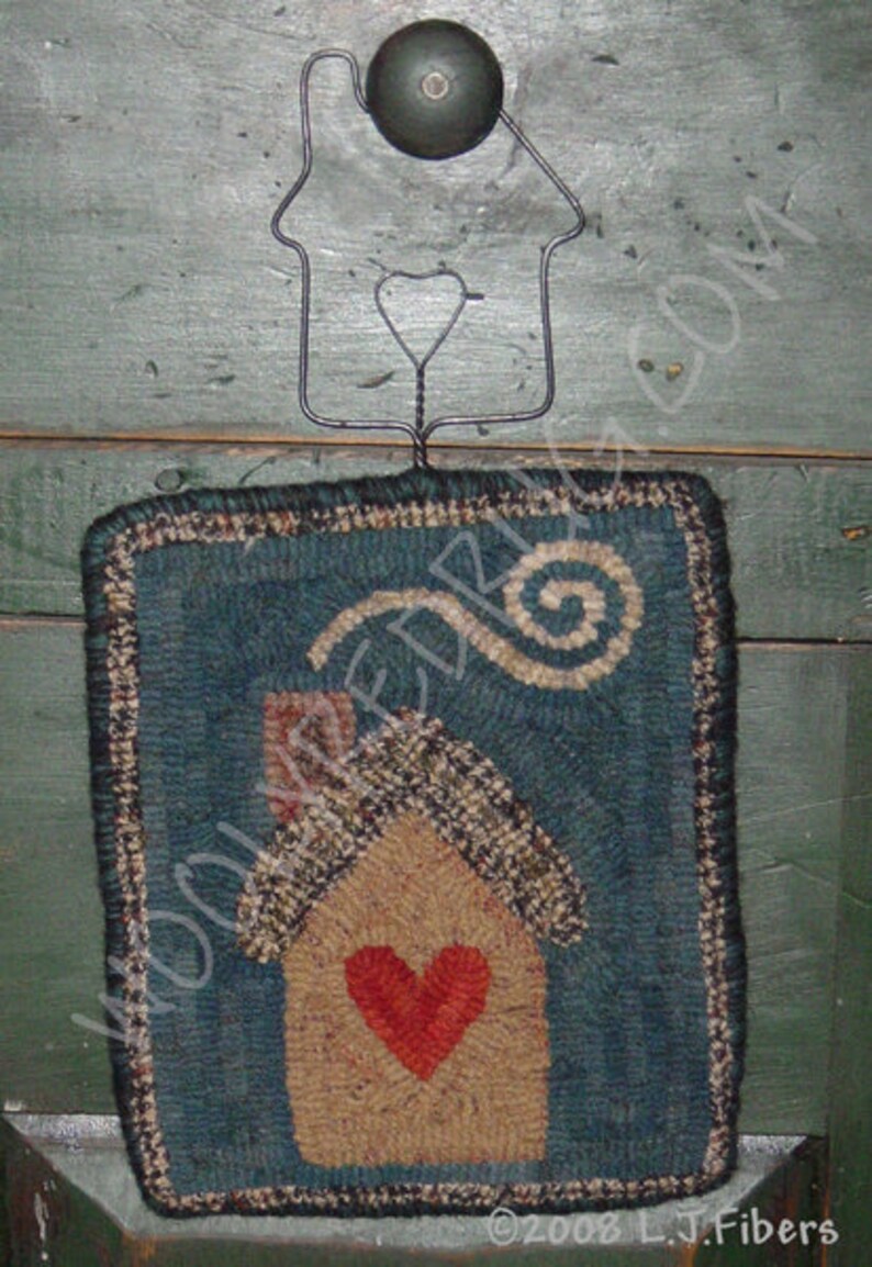 May include: A handcrafted, rectangular wall hanging with a teal background and a house design. The house features a tan body, a red heart, and a patterned roof. A wire house-shaped hanger with a green knob is attached.