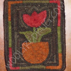 May include: A handmade, square rug with a floral design. The rug features a red tulip in an orange pot, with green leaves. The border is dark brown with green, orange, and red stripes. The text "WOOLYREDRUG.COM" is visible.
