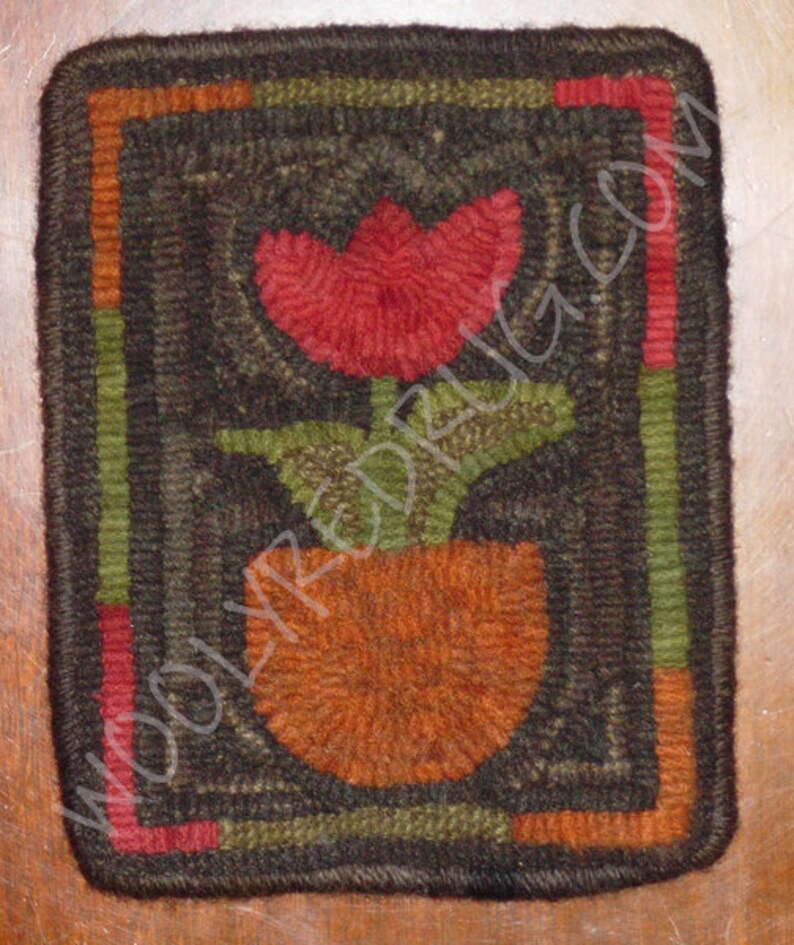 May include: A handmade, square rug with a floral design. The rug features a red tulip in an orange pot, with green leaves. The border is dark brown with green, orange, and red stripes. The text "WOOLYREDRUG.COM" is visible.