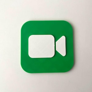 Peut inclure: Un carré vert aux coins arrondis présente une icône de caméra vidéo blanche. L'icône de la caméra est composée d'un rectangle blanc et d'un triangle blanc. Le design est simple et moderne, adapté aux produits liés à la technologie.