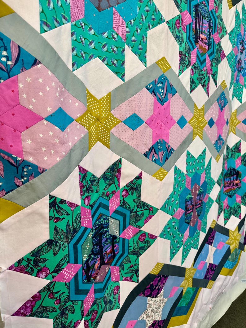 May include: A colorful quilt with a star pattern. The quilt features various fabrics in shades of pink, teal, green, and yellow. The star shapes are outlined with gray fabric. The quilt has a patchwork design.