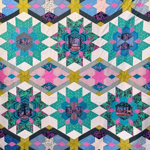 May include: A colorful quilt with a repeating pattern of stars and geometric shapes. The quilt features a variety of colors, including teal, pink, blue, and yellow. The center of each star has a picture of a forest scene.