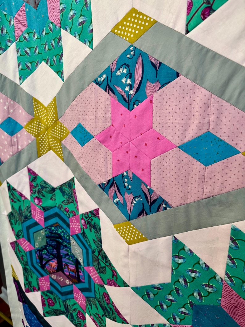 May include: Close-up of a colorful quilt with geometric patterns. The quilt features various shapes, including stars and diamonds, in shades of pink, teal, green, and white. Some sections have floral prints, while others have polka dots.