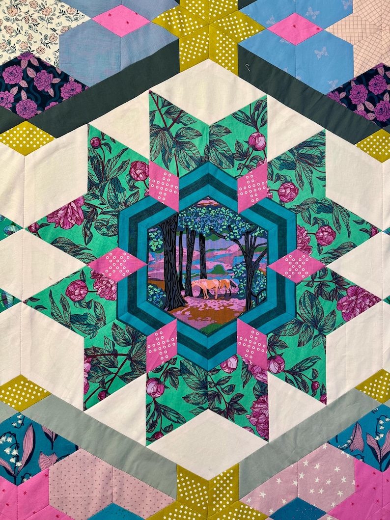 May include: A colorful quilt with a starburst design. The quilt features a central hexagon with a forest scene, surrounded by floral and geometric patterns in shades of pink, green, teal, and white. The quilt is made of various fabric pieces.