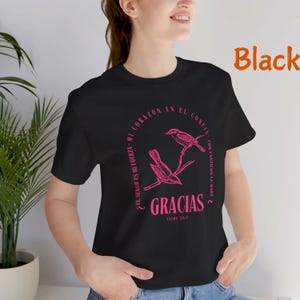 Könnte beinhalten: Schwarzes T-Shirt mit einem rosafarbenen Grafikdesign mit zwei Vögeln auf einem Ast. Der Text "El Señor es mi fuerza-mi corazón en el confía - con cánticos le daré 2" und "Gracias Salmo 28:7" ist auf dem Shirt gedruckt.
