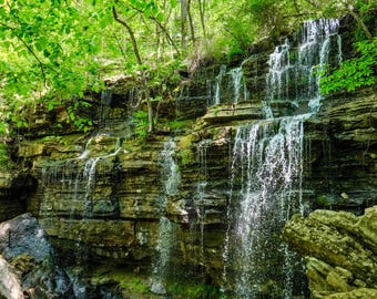 Könnte beinhalten: Ein Wasserfall stürzt über eine Reihe von mit Moos bewachsenen Felsformationen, umgeben von üppigem Grün.