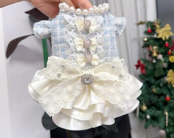 May include: A light blue and white dog dress with a pearl collar and cream-coloured bows. The dress features a lace bodice and a layered skirt with a large bow and rhinestone embellishments. The dress is designed for a small dog.