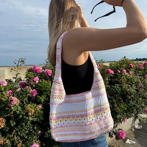 May include: A white crochet tote bag with pink and yellow stripes. The bag has a crocheted design with openwork details.