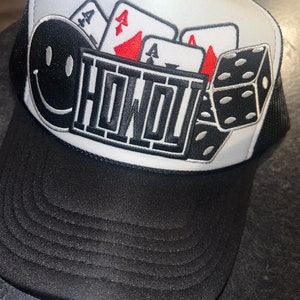 May include: Black and white trucker hat with a smiley face, playing cards, and dice design. The hat features the word "HONDI" in a bold, blocky font. The brim and mesh back are black, and the front panel is white.