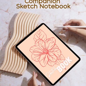 May include: A digital tablet displaying a coral-colored floral sketch, with the words "Sketch Book" and "Flourish Companion Sketch Notebook". A wooden, wave-shaped object and a stylus are also present.