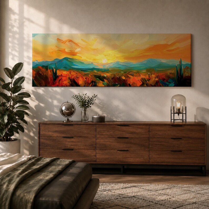 Panoramic desert sunset painting showing distant layered mountains beneath a glowing sun with sweeping orange and gold skies. Thick textured brushstrokes form desert plants and rocky terrain in the foreground while teal and blue ridges fade into the horizon, creating a wide southwestern landscape composition.