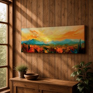 Panoramic desert sunset painting showing distant layered mountains beneath a glowing sun with sweeping orange and gold skies. Thick textured brushstrokes form desert plants and rocky terrain in the foreground while teal and blue ridges fade into the horizon, creating a wide southwestern landscape composition.