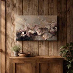 Puede incluir: Una pintura floral abstracta en tonos apagados de beige, rosa y blanco cuelga de una pared de madera. La obra de arte representa delicadas flores y ramas, creando una est&eacute;tica suave y on&iacute;rica. Debajo, un mueble de madera con una planta y un cuenco.