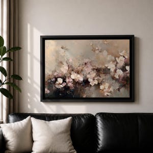 Puede incluir: Pintura floral abstracta en un marco negro. La obra de arte presenta una paleta de colores suaves de blanco, rosa y beige, con pinceladas que crean un efecto texturizado. La pintura se exhibe sobre un sof&aacute; de cuero negro.