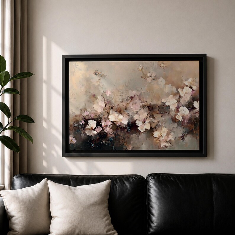 Puede incluir: Pintura floral abstracta en un marco negro. La obra de arte presenta una paleta de colores suaves de blanco, rosa y beige, con pinceladas que crean un efecto texturizado. La pintura se exhibe sobre un sof&aacute; de cuero negro.