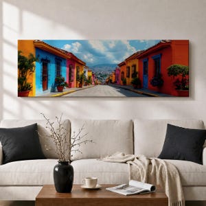 Puede incluir: Un lienzo panor&aacute;mico que muestra una calle estrecha bordeada por edificios de colores vibrantes en tonos azul, naranja, amarillo y rojo. La escena incluye plantas en macetas, puertas de madera oscura y una vista de una monta&ntilde;a lejana.