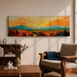 Panoramic desert sunset painting showing distant layered mountains beneath a glowing sun with sweeping orange and gold skies. Thick textured brushstrokes form desert plants and rocky terrain in the foreground while teal and blue ridges fade into the horizon, creating a wide southwestern landscape composition.