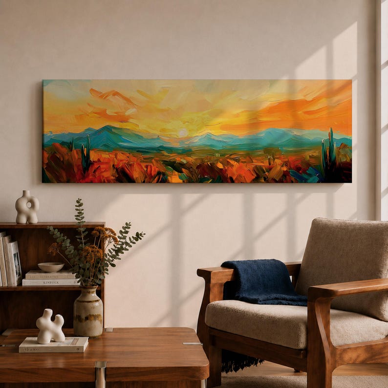 Panoramic desert sunset painting showing distant layered mountains beneath a glowing sun with sweeping orange and gold skies. Thick textured brushstrokes form desert plants and rocky terrain in the foreground while teal and blue ridges fade into the horizon, creating a wide southwestern landscape composition.
