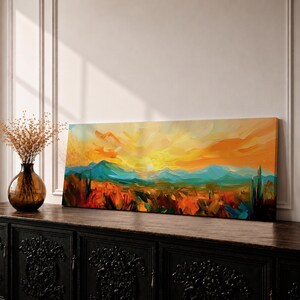 Panoramic desert sunset painting showing distant layered mountains beneath a glowing sun with sweeping orange and gold skies. Thick textured brushstrokes form desert plants and rocky terrain in the foreground while teal and blue ridges fade into the horizon, creating a wide southwestern landscape composition.
