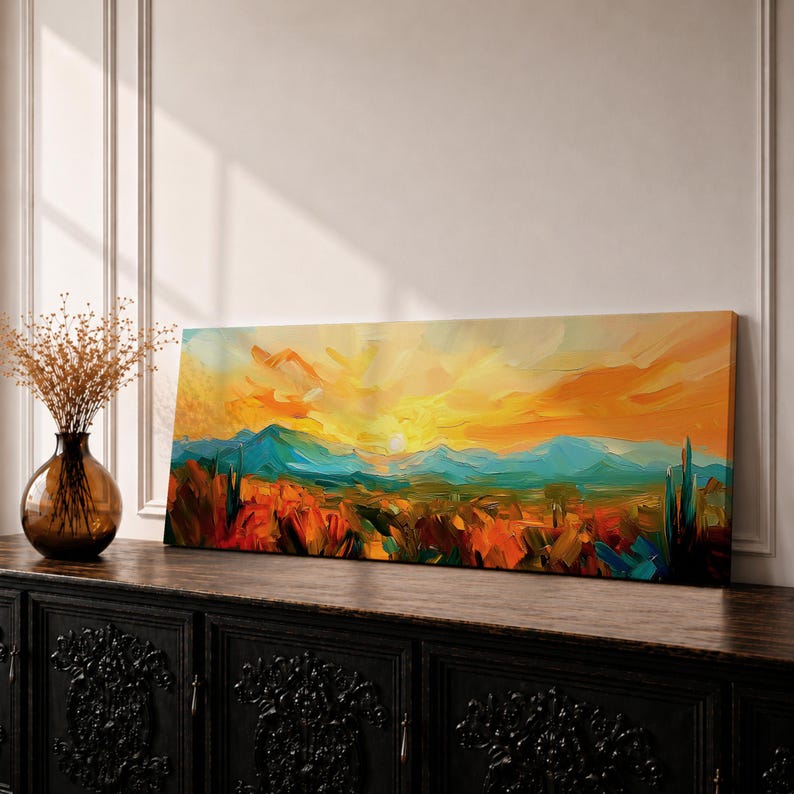 Panoramic desert sunset painting showing distant layered mountains beneath a glowing sun with sweeping orange and gold skies. Thick textured brushstrokes form desert plants and rocky terrain in the foreground while teal and blue ridges fade into the horizon, creating a wide southwestern landscape composition.