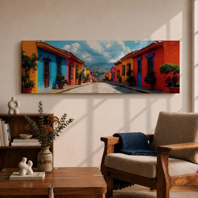 Puede incluir: Un cuadro panor&aacute;mico que representa una calle estrecha bordeada por edificios de colores vibrantes en tonos naranja, azul, amarillo y rojo. La escena incluye plantas en macetas, puertas de madera oscura y una monta&ntilde;a bajo un cielo nublado.
