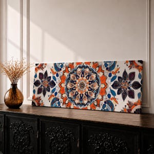 Könnte beinhalten: Ein rechteckiges Wandbild auf Leinwand mit einem zentralen, kreisförmigen Mandalamuster in den Farben gebranntes Orange, Dunkelblau und Creme. Das Design umfasst symmetrische Blumenmotive und komplexe geometrische Formen auf der gesamten Fläche.