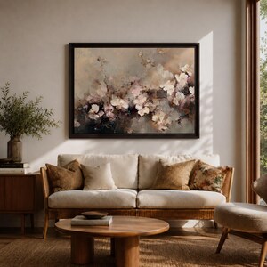 Puede incluir: Una pintura floral enmarcada con un marco marr&oacute;n oscuro cuelga sobre un sof&aacute; color crema. La pintura presenta flores blancas y rosas con un fondo apagado. El sof&aacute; tiene cojines marrones y un marco de madera. Una mesa de centro de madera est&aacute; frente al sof&aacute;.