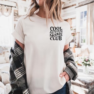 Może przedstawiać: Biała koszulka z czarnym nadrukiem "Cool Autism Moms Club".