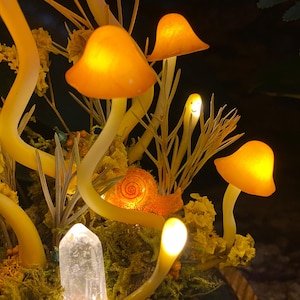 Puede incluir: Una escena de bosque de ensue&ntilde;o con hongos naranjas brillantes, un caracol y un cristal de cuarzo transparente. Los hongos est&aacute;n hechos de vidrio y tienen un brillo c&aacute;lido y acogedor. El caracol es un elemento decorativo que agrega un toque de fantas&iacute;a a la escena. El cristal de cuarzo es un elemento natural que agrega un toque de brillo a la escena.