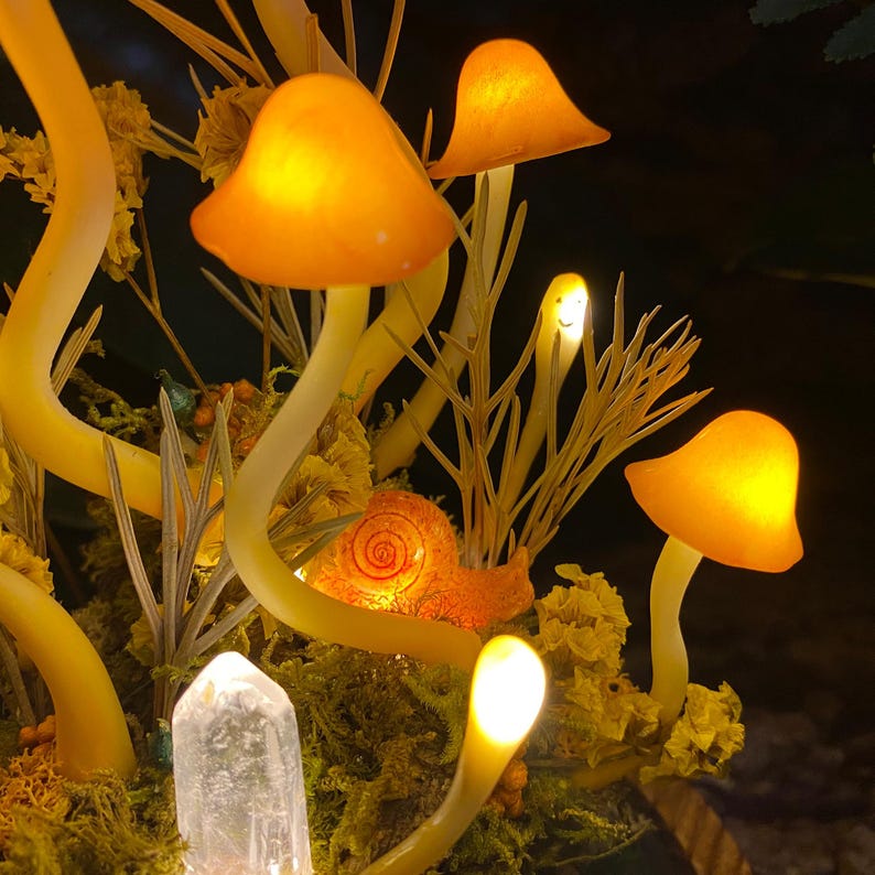 Puede incluir: Una escena de bosque de ensue&ntilde;o con hongos naranjas brillantes, un caracol y un cristal de cuarzo transparente. Los hongos est&aacute;n hechos de vidrio y tienen un brillo c&aacute;lido y acogedor. El caracol es un elemento decorativo que agrega un toque de fantas&iacute;a a la escena. El cristal de cuarzo es un elemento natural que agrega un toque de brillo a la escena.