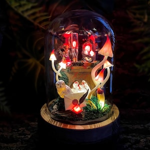 May include: A whimsical, illuminated glass dome featuring a miniature fantasy scene. Inside, glowing mushrooms, an owl, and other magical elements are arranged. The base is wooden, and the scene is lit with red and white lights, creating a warm, enchanting ambiance.