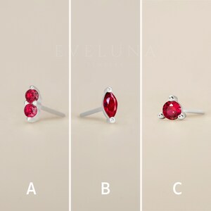 May include: Three different styles of earrings with red gemstones. The first pair features two round red gemstones, the second pair features a single marquise-shaped red gemstone, and the third pair features a single round red gemstone surrounded by three smaller gemstones.