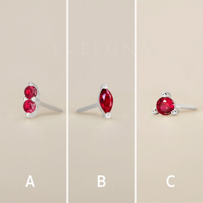 May include: Three different styles of earrings with red gemstones. The first pair features two round red gemstones, the second pair features a single marquise-shaped red gemstone, and the third pair features a single round red gemstone surrounded by three smaller gemstones.