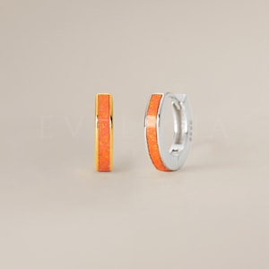 May include: A pair of small hoop earrings with a thin band of orange opal. The earrings are available in gold and silver.