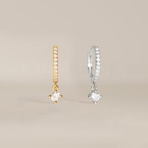 May include: A pair of hoop earrings with a dangling crystal. The earrings are available in gold and silver.