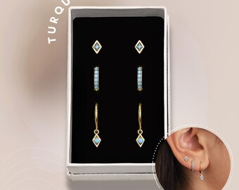 May include: A set of turquoise earrings in a white box. The set includes a pair of small square earrings, a pair of hoop earrings with turquoise stones, and a pair of dangle earrings with turquoise stones.