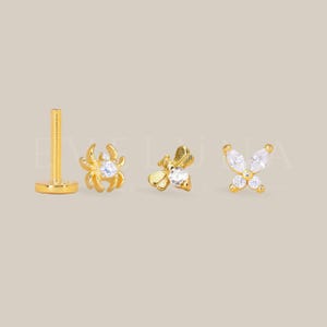 May include: Gold-colored earrings with insect and butterfly designs. The earrings include a spider, a bee, and a butterfly, each adorned with a central clear gemstone. The earring posts are also gold-colored.