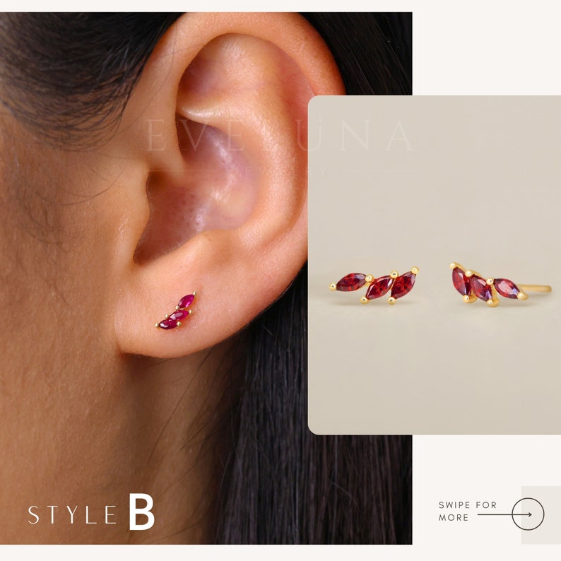 Op de afbeelding: Een paar gouden oorbellen met drie rode, marquisevormige edelstenen. De oorbellen worden getoond op het oor van een model.