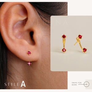 Op de afbeelding: Twee paar oorbellen met rode edelstenen. Het ene paar is een enkele oorbel met een rode edelsteen, het andere paar is een gebogen staaf met twee rode edelstenen.