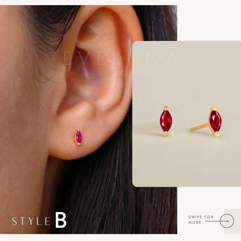 May include: A pair of gold earrings with small red marquise-shaped gemstones. The earrings are shown on a model's ear.