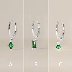 May include: Three silver hoop earrings with different green gemstone pendants. The earrings are labeled A, B, and C. Each earring has a different gemstone shape: a diamond, a rectangle, and a round shape. The brand name "EVELUNA JEWELRY" is in the background.