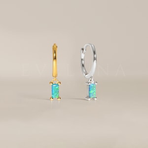 Puede incluir: Un par de pendientes de aro con una piedra de ópalo rectangular colgante. Los pendientes están disponibles en oro y plata.