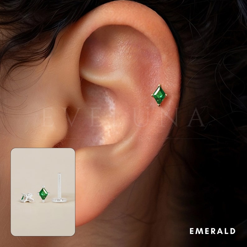 Może przedstawiać: Zbliżenie na srebrny kolczyk z zielonym szmaragdowym kamieniem szlachetnym. Kolczyk jest pokazany w uchu modelki.