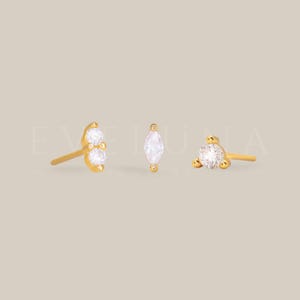 Peut inclure: Trois boucles d'oreilles dorées avec des pierres en oxyde de zirconium claires et étincelantes. Une boucle d'oreille comporte deux pierres, une autre une pierre de forme marquise et la troisième une pierre ronde. Bijoux.